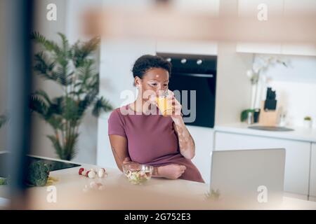 Una donna dalla pelle scura che beve un succo d'arancia Foto Stock