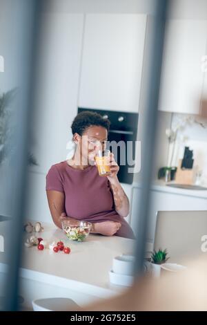 Una donna dalla pelle scura che beve un succo d'arancia Foto Stock