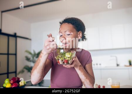 Una giovane donna con pigmentazione sul viso mangiare insalata Foto Stock