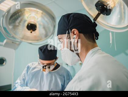 Medici che lavorano in sala operatoria presso la clinica ospedaliera - Focus sul volto maschile destro Foto Stock