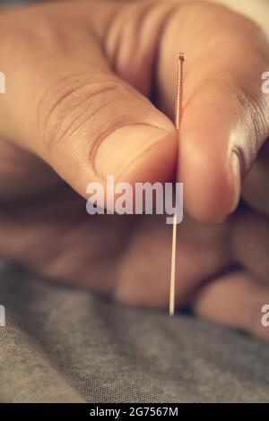 Mani di un medico che tiene un ago di agopuntura maneggiato di rame. Medicina alternativa cinese. Trattamento di malattie con aghi. Foto Stock