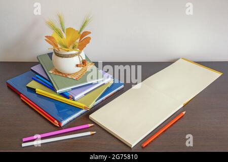 Concetto scolastico. Pila di libri, matite colorate colorate e album di schizzo aperto su sfondo scuro. Foglie d'autunno. Spazio libero per testo o foto Foto Stock