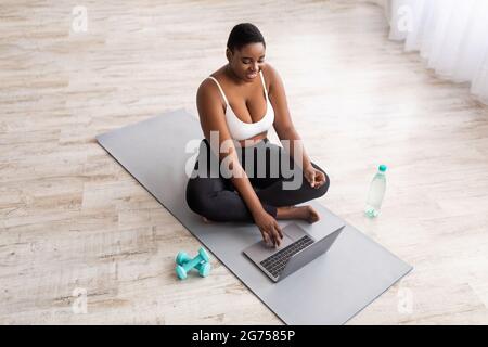 Donna nera più grande che guarda video di sport online sul laptop prima di allenarsi a casa, sopra la vista Foto Stock