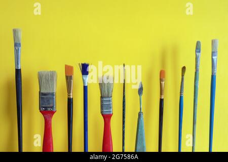 Diversi pennelli di vernice su sfondo di carta giallo. Spazio di copia Foto Stock