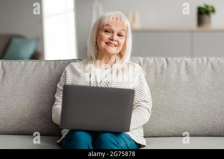 Donna matura seduta sul divano e che usa il computer Foto Stock