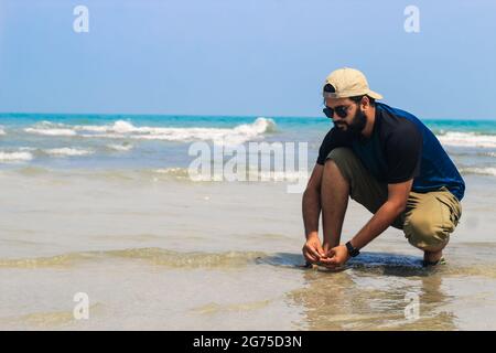 Il giovane al mare raccoglie conchiglie sulla spiaggia, tramonto, vacanze estive in mare o in oceano. Un ragazzo sulla spiaggia che raccoglie conchiglie. Foto Stock