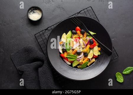 Pasta a grani interi con verdure su un piatto bianco su fondo nero di ardesia, pietra o calcestruzzo. Vista dall'alto con spazio per la copia. Foto Stock