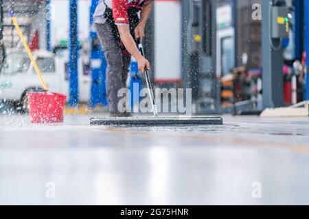 il personale addetto alla manutenzione utilizza un mop per rimuovere l'acqua nella pulizia uniforme degli indumenti protettivi del nuovo pavimento epossidico in un magazzino vuoto o in un vano auto Foto Stock