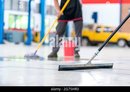 Selezionare il mop di messa a fuoco, l'addetto alla manutenzione utilizzando un mop per rimuovere l'acqua nella pulizia uniforme degli indumenti protettivi del nuovo pavimento epossidico in un vuoto Foto Stock