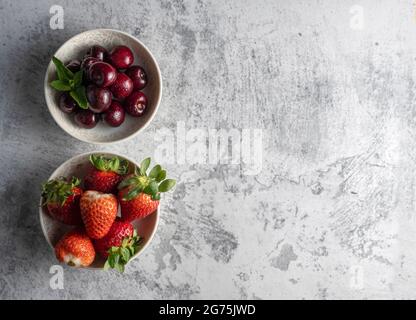 Piccole ciotole piene di fragole e ciliegie poste su sfondo bianco. Sensazione di freschezza e frutta succosa. Foto Stock