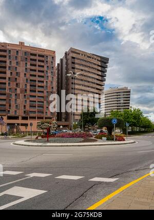 Particolare di viale con edifici in un'area urbana con un cielo nuvoloso al tramonto. Area paesaggistica con fiori, alberi e arbusti. Foto Stock