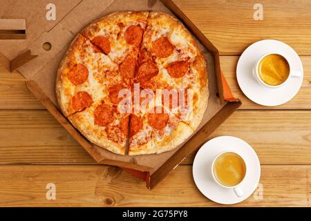 Pizza pepperoni in scatola aperta e due tazze di caffè espresso su tavolo di legno. Vista dall'alto. Foto Stock