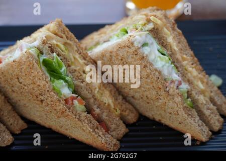 Due panini club posti su un piatto nero in un ristorante. Foto ravvicinata di un sandwich club. Sandwich con prosciutto, verdure, lattuga e mayo Foto Stock