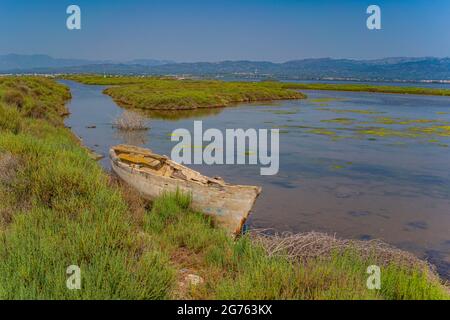 Canale d'acqua attraverso i campi di riso con una barca di legno marcio al Delta di Ebro nella regione di Tarragona. Spagna Foto Stock