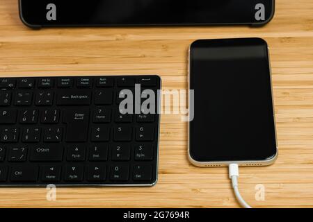 Lo smartphone si sta caricando accanto al tablet e alla tastiera. Foto Stock