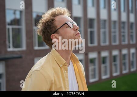 Giovane uomo pensivo con occhi chiusi che respirano aria fresca, rilassandosi nel parco. Concetto di detox digitale Foto Stock