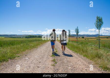 Una bella coppia che cammina attraverso la strada tra i campi verdi in estate Foto Stock