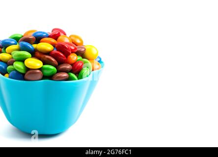 Bottoni di cioccolato color arcobaleno rivestiti con caramelle in una ciotola blu divertente su sfondo bianco Foto Stock