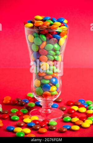 Un vetro riempito con bottoni di cioccolato color arcobaleno con rivestimento di caramelle Foto Stock