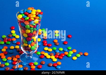 Un vetro riempito con bottoni di cioccolato color arcobaleno con rivestimento di caramelle Foto Stock