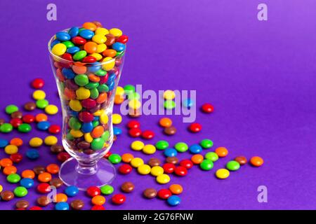 Un vetro riempito con bottoni di cioccolato color arcobaleno con rivestimento di caramelle Foto Stock
