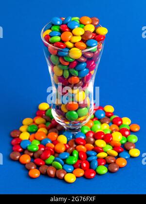 Un vetro riempito con bottoni di cioccolato color arcobaleno con rivestimento di caramelle Foto Stock