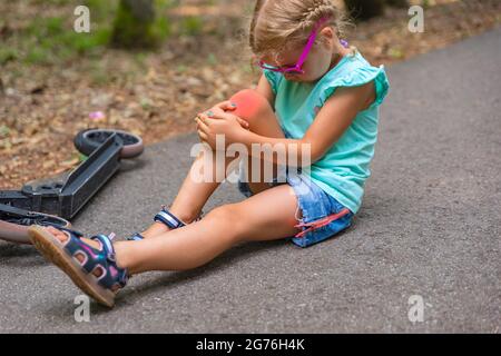 Trauma su scooter. Una bambina di cinque anni cadde su uno scooter in un parco e le ferì gravemente il ginocchio. Concetto di lesioni da scooter elettrico Foto Stock