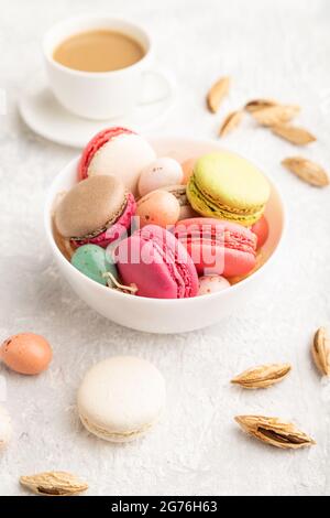 Macaroni multicolore e uova di cioccolato in ciotola di ceramica, tazza di caffè su fondo grigio di cemento. Vista laterale, primo piano, vita still. Colazione, mattina Foto Stock