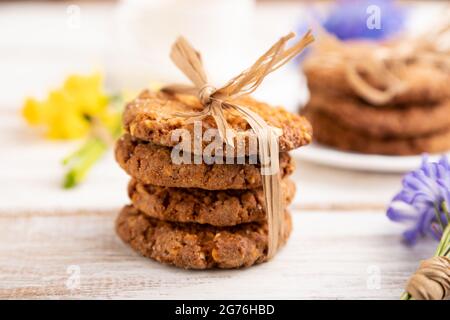 Biscotti di farinata d'avena con fiori primaverili alle narciso, narciso e tazza di caffè su sfondo di legno bianco. Vista laterale, primo piano, sfocato, fermo Foto Stock