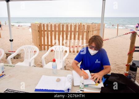 Un volontario del gruppo per lo studio e la protezione degli ecosistemi catalani - ecologi della Catalogna (GEPEC-EDC) siede accanto al nido di sabbia recintato dove la tartaruga della testa di loggerhead ha generato le sue uova.UNA tartaruga della testa di loggerhead (Caretta caretta), in grave pericolo di estinzione, Siamo arrivati alla spiaggia di Calafell il 19 giugno per deporre 161 uova in un nido fatto nella sabbia. La polizia locale di Calafell ha preso 61 delle uova al CRAM (Centro per la conservazione e il recupero degli animali marini) A causa della necessità di un incubatore e il resto delle uova nel nido sono custodite 24 ore fino a quando non schiudono dal Gruppo per lo Stu Foto Stock