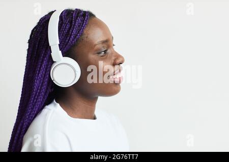 Vista laterale ritratto di giovane afroamericana indossando cuffie su sfondo bianco, spazio copia Foto Stock