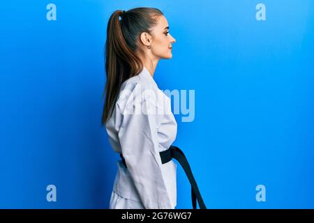 Bella bruna giovane donna che indossa divisa da combattimento karate con cintura nera che guarda a lato, profilo relax posa con viso naturale con smi sicuro Foto Stock