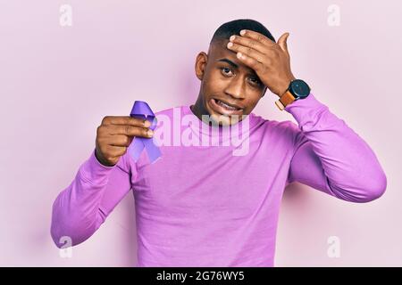 Giovane uomo nero che tiene la consapevolezza del nastro viola stressato e frustrato con la mano sulla testa, sorpresa e faccia arrabbiata Foto Stock