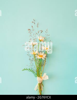 Bouquet accogliente di fiori di camomilla con erba rurale su sfondo turchese. Concetto minimalista. Foto Stock