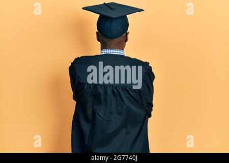 Il giovane afroamericano indossa il cappuccio di graduazione e la cerimonia si levano in piedi indietro guardando via con le braccia incrociate Foto Stock