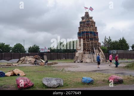 Belfast, Regno Unito. 11 Luglio 2021. Tre uomini passano davanti a un falò con una bandiera Union Jack e Ulster attaccata alla cima.per celebrare la battaglia del Boyne, i falò sono costruiti in vari quartieri protestanti in tutta Belfast. I falò sono accesi la notte prima delle dodici sfilate di luglio, l'11 luglio. (Foto di Natalia Campos/SOPA Images/Sipa USA) Credit: Sipa USA/Alamy Live News Foto Stock