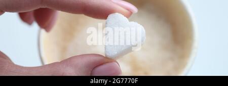 Donna che mette il cubetto di zucchero del caffè a forma di closeup del cuore Foto Stock