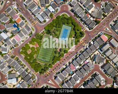 Tiro drone diretto di campo da calcetto vuoto e campo tenis circondato da parco e alberi in una comunità recintata fuori Guayaquil City, Ecuador. Foto Stock