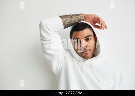 Ritratto minimale di giovane uomo tatuato con cappuccio bianco e guardando la fotocamera, copia spazio Foto Stock