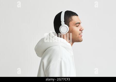 Ritratto con vista laterale minima di un uomo latino-americano moderno che indossa le cuffie con cappuccio bianco mentre ascolti la musica, spazio per la copia Foto Stock