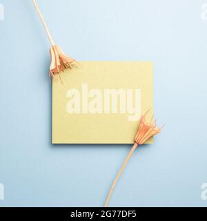 Memo pad giallo con fiori secchi rosa su sfondo blu. Vista dall'alto, spazio per la copia Foto Stock