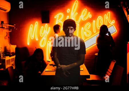 Un uomo che indossa un cappello di stoffa, affascinante e feroce eyes.Under le luci al neon e dietro le lettere della mia bici leggera Foto Stock