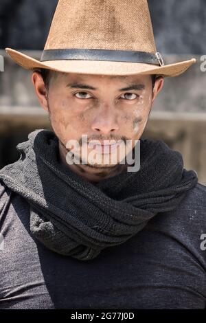 Uomo attraente la faccia è sporca con macchie di terreno e cement.behind le scene lavorano porta. Operaio indossando un cappello con una sciarpa nera elegante Foto Stock