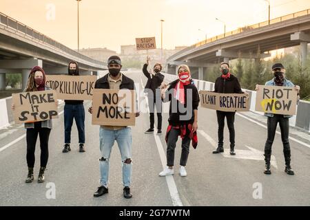 Gruppo di giovani multietnici in maschere di stoffa in piedi sulla strada mentre protestando sulla strada Foto Stock