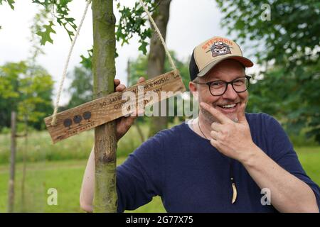 Amburgo, Germania. 09 luglio 2021. Jan Schierhorn, fondatore della Fame Forest, sorge accanto a una quercia da palude appena piantata nella Fame Forest, sulla quale è appesa una targa di legno con l'iscrizione '50 anni Warner Music Group Germany 1971 - 2021'. La Barclaycard Arena ha creato un monumento in crescita al gruppo Warner Music nella Fame Forest di Amburgo per celebrare il suo 50° anniversario. (Per dpa 'la società musicale Warner Music ottiene un albero Fame Forest per segnare il suo 50 °'). Credit: Marco Brandt/dpa/Alamy Live News Foto Stock