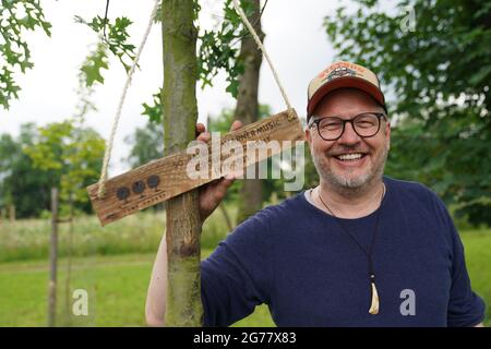 Amburgo, Germania. 09 luglio 2021. Jan Schierhorn, fondatore della Fame Forest, sorge accanto a una quercia da palude appena piantata nella Fame Forest, sulla quale è appesa una targa di legno con l'iscrizione '50 anni Warner Music Group Germany 1971 - 2021'. La Barclaycard Arena ha creato un monumento in crescita al gruppo Warner Music nella Fame Forest di Amburgo per celebrare il suo 50° anniversario. (Per dpa 'la società musicale Warner Music ottiene un albero Fame Forest per segnare il suo 50 °'). Credit: Marco Brandt/dpa/Alamy Live News Foto Stock