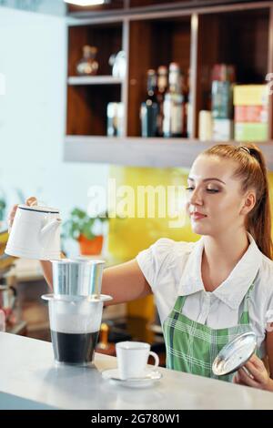 Barista femminile che versa acqua calda nel filtro phin quando si prepara un caffè vietnamita per il cliente Foto Stock