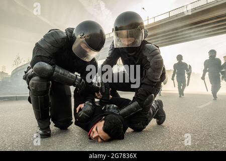 Poliziotto forte in caschi torcendo le braccia del protetore dietro la schiena mentre lo ferma in strada Foto Stock