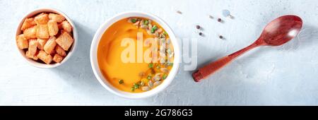 Panorama della zuppa di zucca piccante con crostini, punto di posa piano in alto con un cucchiaio di legno Foto Stock