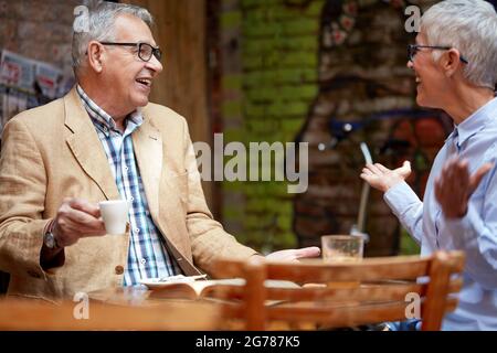 coppia caucasica senior che parla in un caffè all'aperto, sorridendo, bevendo caffè, guardandosi l'un l'altro Foto Stock